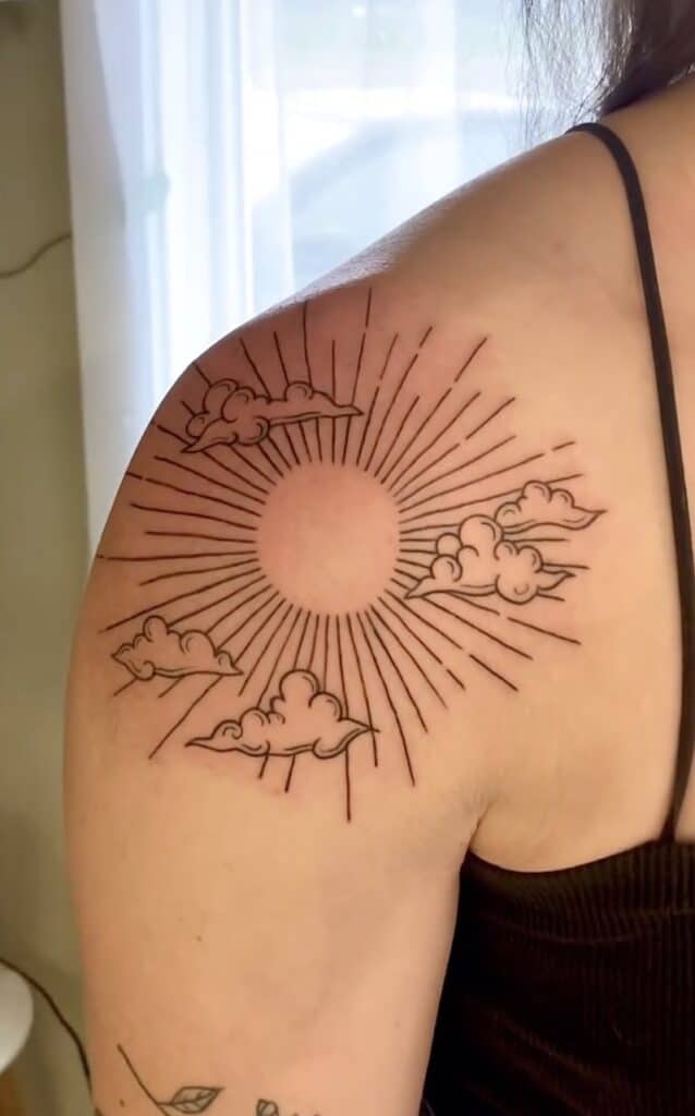 Minimalistic sun with clouds tattoo design on shoulder for art lovers.