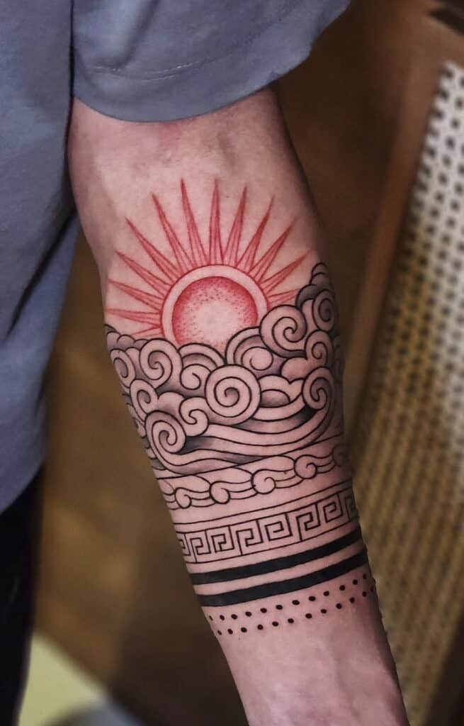 Alt text: Artistic tattoo of a sunrise with clouds and geometric patterns on arm.
