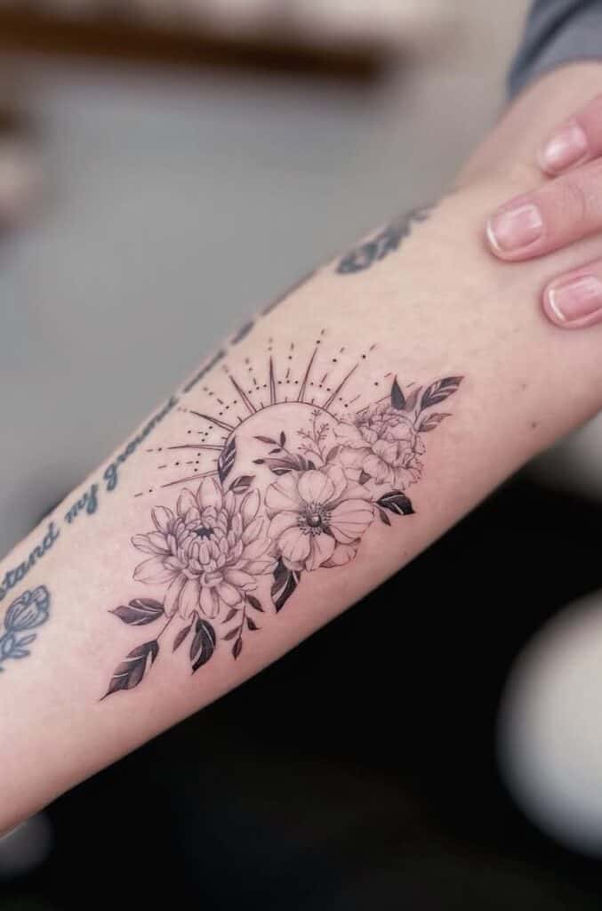 Delicate floral tattoo with sun rays on person's forearm, black outline, artistic sketch style.