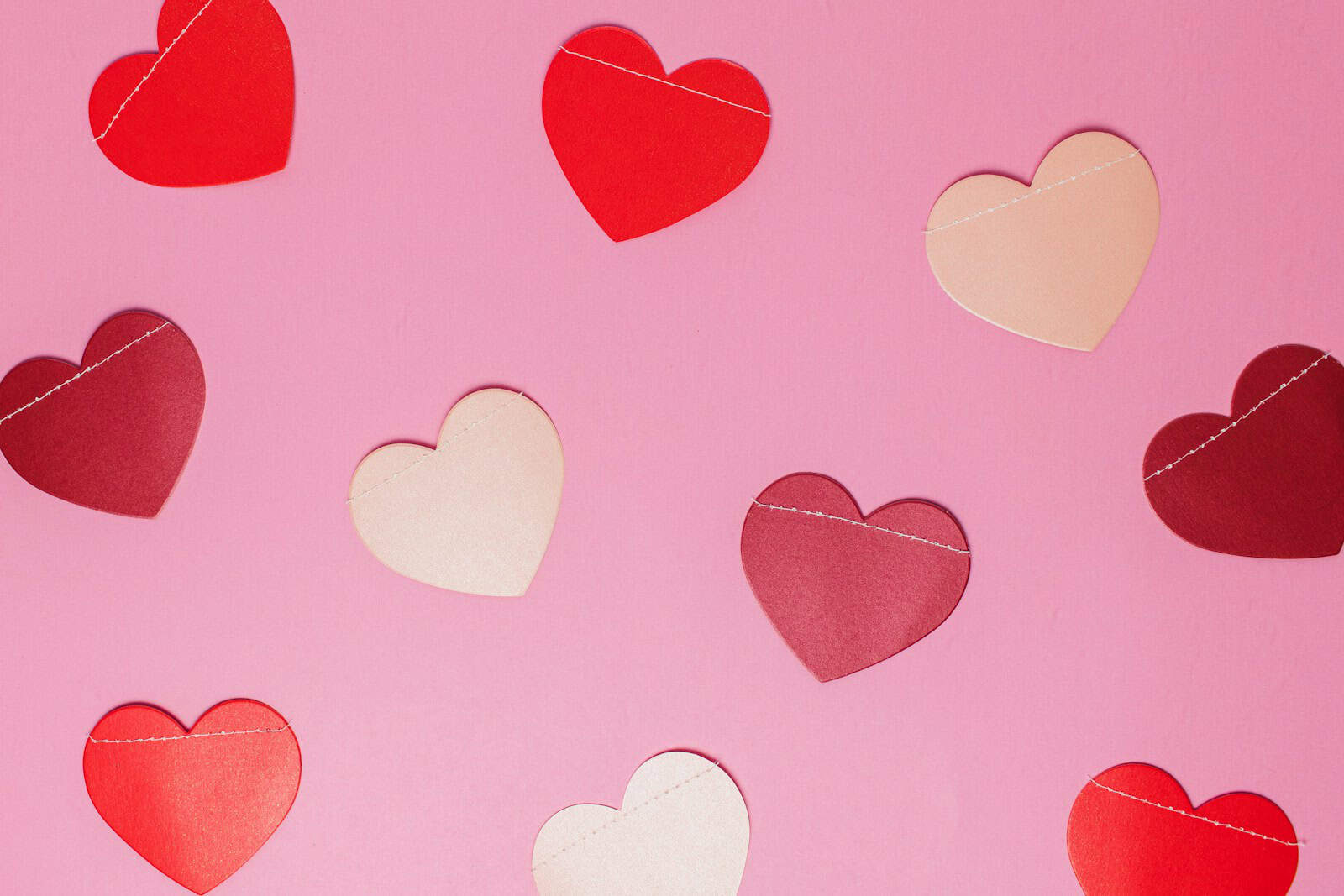 Colorful paper heart cutouts on pink background for crafts and celebrations.
