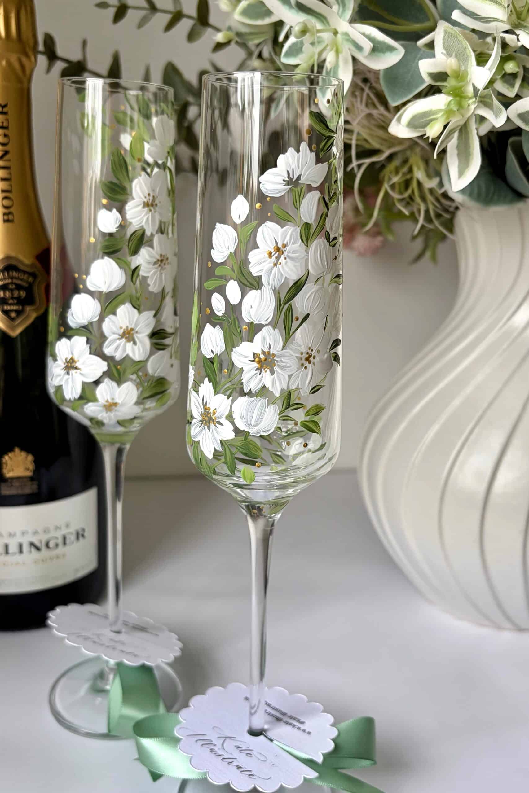 Beautiful hand-painted floral wine glasses with white blossoms and green leaves.