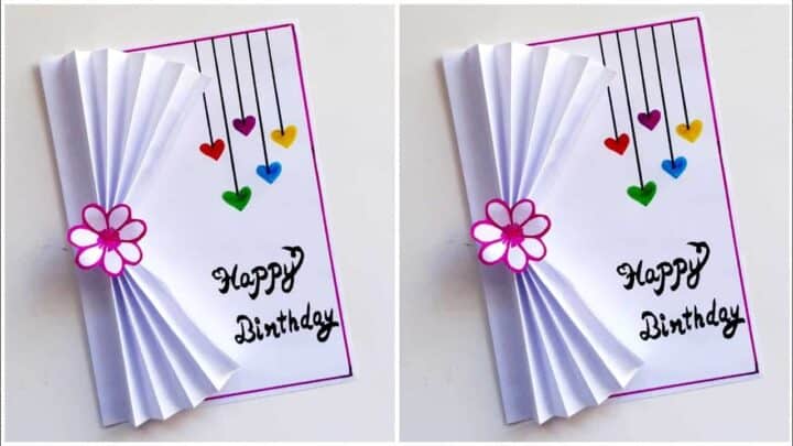 Creative handmade birthday card with paper fan, flower, and hanging hearts.