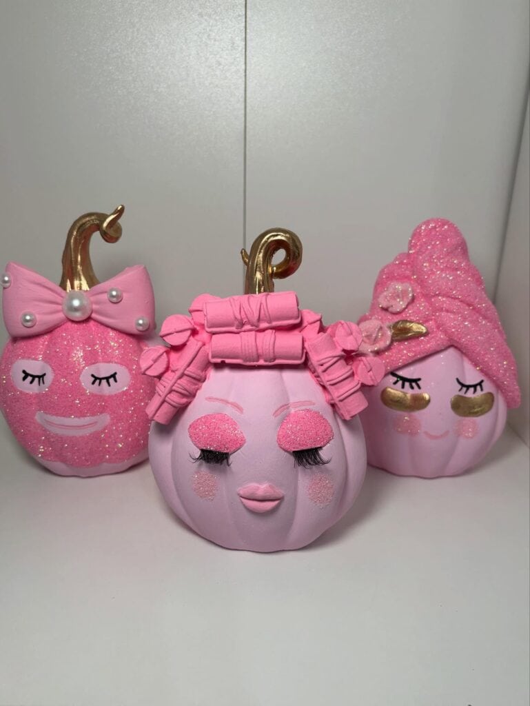 Three pink pumpkin decorations with bows, eyelashes, and gold accents for fall.