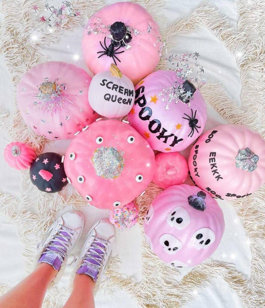 Colorful pink pumpkins decorated with spiders, glitter, and spooky messages for Halloween.