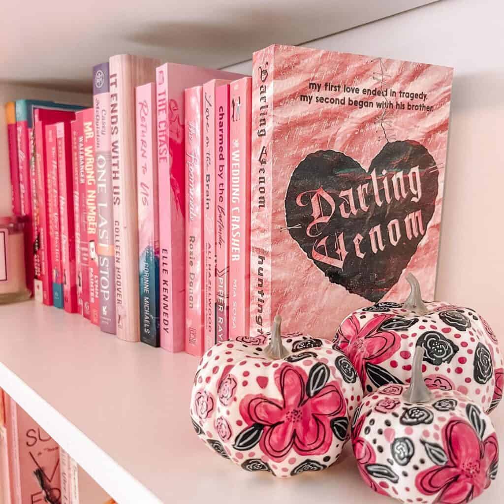 Decorative pink pumpkins with black and pink floral patterns beside a row of pink books.