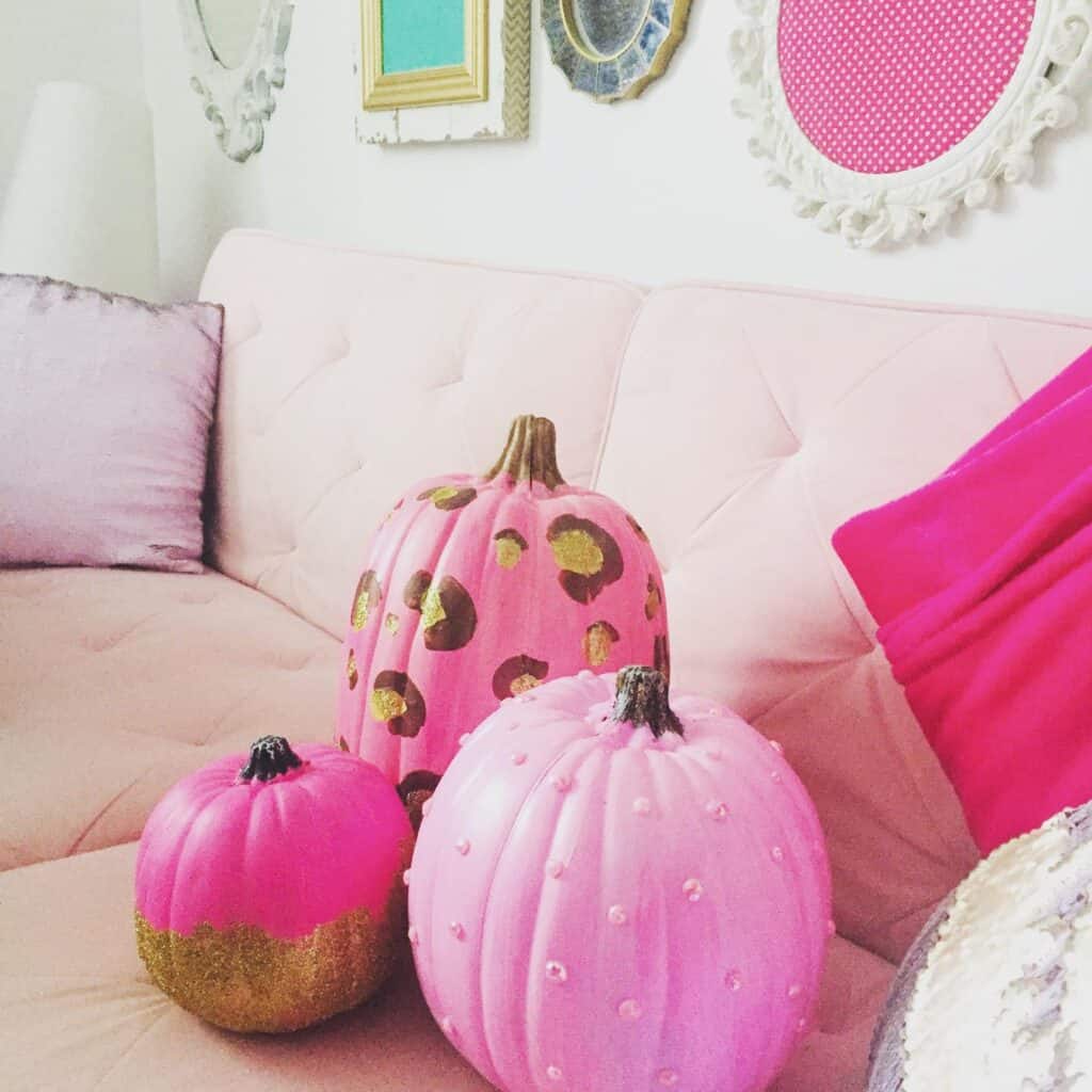 Decorative pink pumpkins with gold and pearl accents on a pastel sofa.
