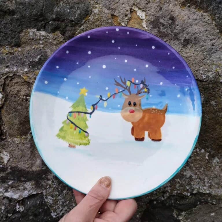Decorative Christmas plate with reindeer and Christmas tree scene.