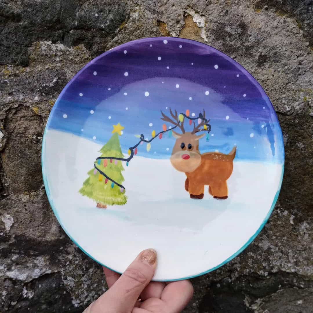 Decorative Christmas plate with reindeer and Christmas tree scene.
